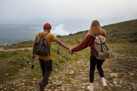 A couple on a hiking trip holding hands, photo from behind.