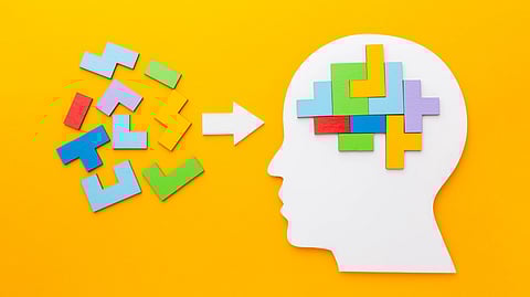 Silhouette of a head filled with colorful, interlocking puzzle pieces against a yellow background.