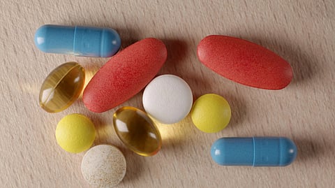 A variety of pills and capsules lie on a wooden surface. 