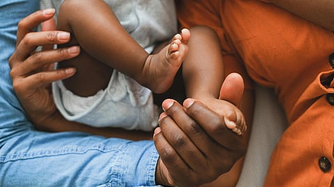 Close-up of adult hands gently holding an infant's legs.