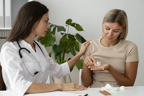 A lady doctor is giving some tablets to another young woman.