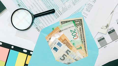 currency notes kept in middle, magnifying glass on side and bills scattered around.