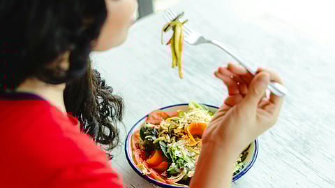 A person in a red shirt is eating a colorful salad with zucchini strips using a fork.