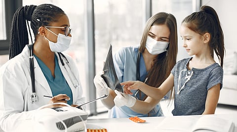 A doctor and nurse, both in masks, are showing an X-ray to a young girl in a clinic. 