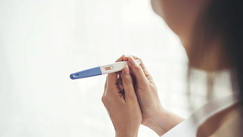A person holds a pregnancy test showing two pink lines, indicating a positive result.