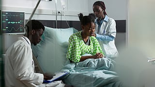 A doctor listens to a patient's back with a stethoscope in a hospital room.