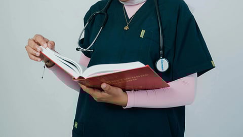 A doctor in scrubs studying from a book and stethoscope around neck,
