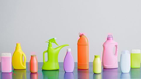 A row of colorful plastic detergent bottles on a blue surface against a gray background, representing household cleaning products.