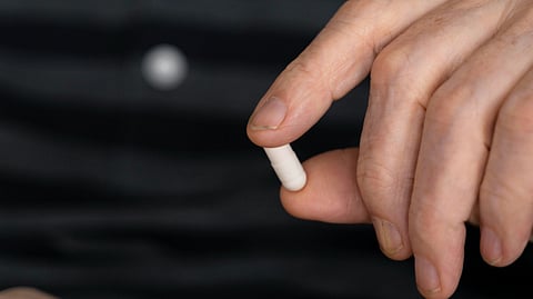 An elderly person holding a white pill and some red pills in their palm.