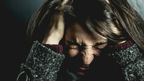 A woman clutches her head in frustration, eyes closed tightly. 