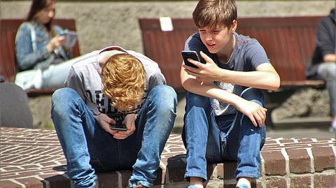 Two boys sit on a brick ledge focused on their smartphones. 