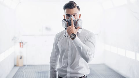 A man in a white shirt wears a gas mask in a bright space, showing air purification.