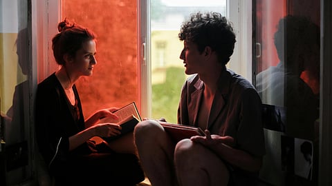 Two people sit in a cozy window nook, talking to each other.