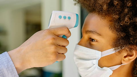 A young person wearing a mask gets a temperature check with a handheld thermometer at an entrance.