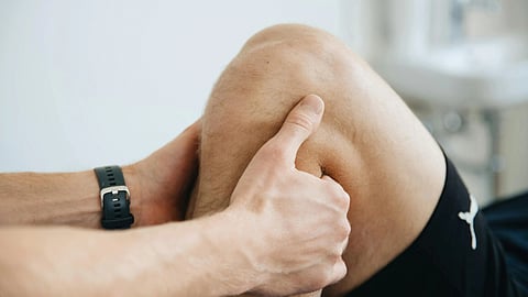 A person’s hand firmly holds a bent knee, possibly indicating a massage or physical therapy session. 