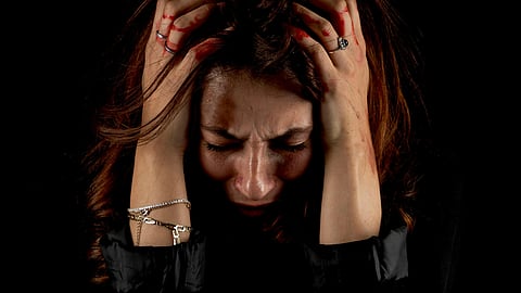 A woman in emotional distress clutches her head with both hands, eyes closed.