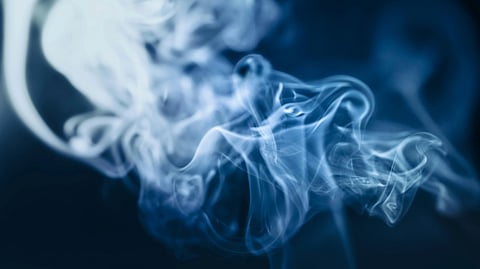 Wispy, blue-tinged smoke curls and swirls against a dark background.
