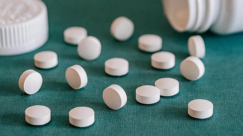 White round pills scattered on a teal surface next to an open bottle.