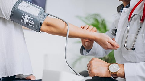 A doctor in a white coat checks a patient's blood pressure using a cuff. 