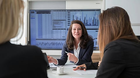 A woman in a business suit leads a meeting in a boardroom.