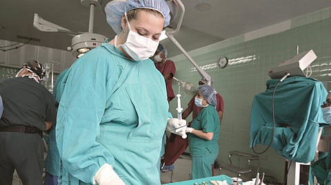 A surgical team in an operating room, focused and wearing teal scrubs and masks.
