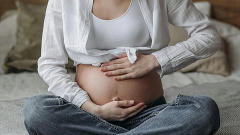 Pregnant woman in a white shirt and jeans sits cross-legged on a bed.