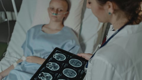 A doctor in a white coat shows brain scans on a tablet to a young patient in a hospital bed.