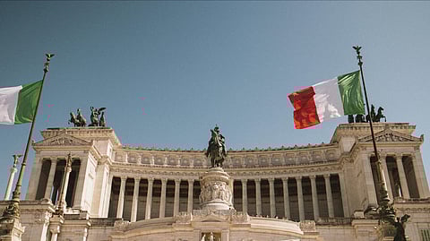 Italian building with statue in middle and Italian flags on both sides.