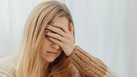 Woman in a cozy sweater sits on a cushion, resting her head in her hand.