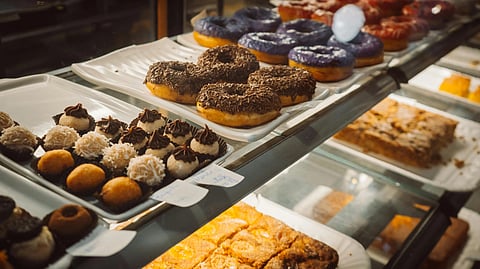 Bakery display with assorted colorful donuts and chocolate-topped pastries on white trays. 