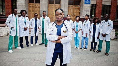 A confident female doctor stands arms crossed in front of a diverse group of medical professionals.