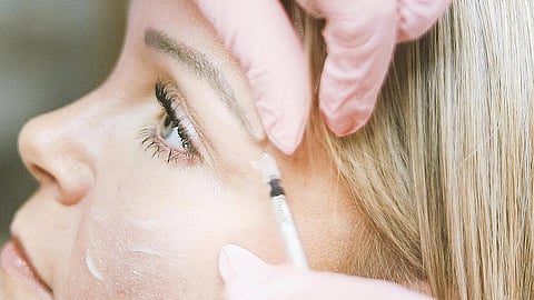 A woman receives a cosmetic facial injection from a professional wearing pink gloves.