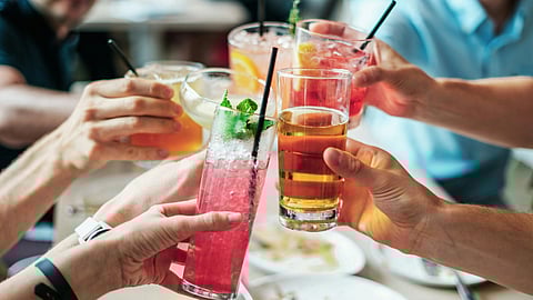A group of people clinking colorful drinks in a cheerful toast, showing joy and camaraderie.