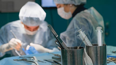 Two surgeons in sterile gowns and masks operate in a brightly lit room.