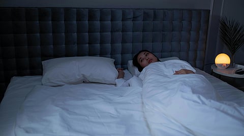 A person lies awake in bed under a white blanket, gazing upwards. 
