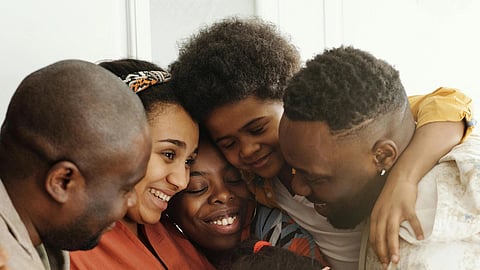 A diverse group of six people share a warm group hug, smiling and joyful. 