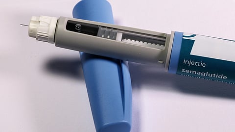 A gray and blue medical injection pen labeled "semaglutide," resting on its blue cap. 