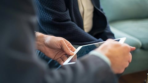 Two people sit on a sofa, holding a tablet.