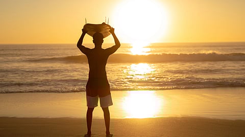 Silhouette of a person on a beach at sunset, holding a red crab overhead.