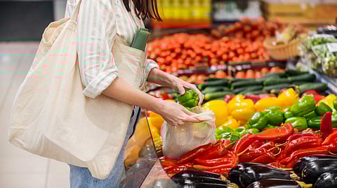 A person places green peppers into a reusable bag at a colorful produce section in a grocery store. 