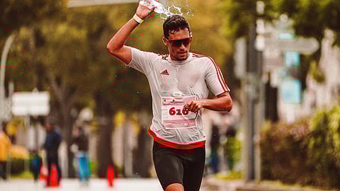 Runner in a white and red shirt splashes water on his head during a race.