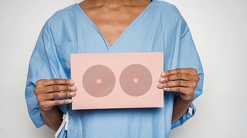 Person in a blue hospital gown holds a pink paper with two circular breast illustrations.