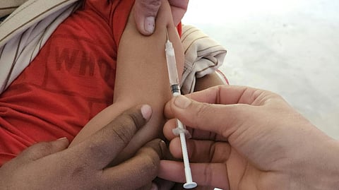 A child receiving a vaccination in the arm, with a healthcare worker's hand holding the syringe. 
