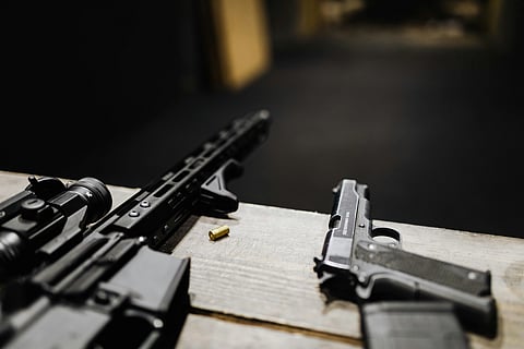 A rifle and a handgun lie on a wooden table indoors.