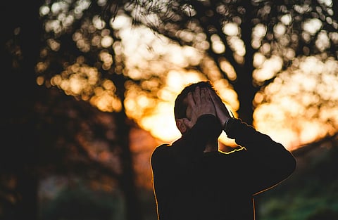 A person outdoors at sunset covering their face with their hands, conveying emotional stress and mental overwhelm.