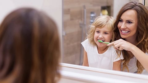 A girl child is being helped by her mother to brush. 