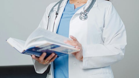 A doctor with stethoscope around neck and book in hand.