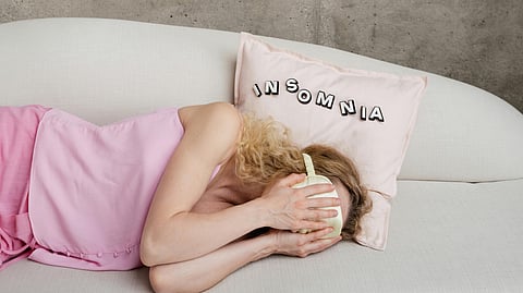 Women in pink pyjamas, on bed, covering face.