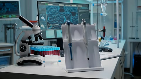 A laboratory workstation featuring a microscope, test tubes, and pipettes with a computer monitor displaying scientific data.