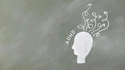 Chalk drawing of a head with "ADHD" written beside it on a chalkboard. Curved arrows emerge from the head.